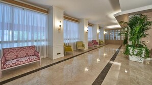 A spacious lobby with a marble floor, a pink sofa, and several chairs. - Hotel Astoria (Biella)