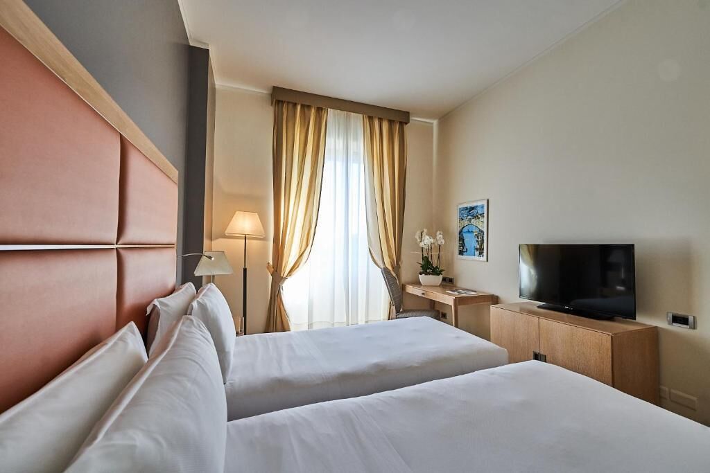 Une chambre d’hôtel avec deux lits, une télévision, un bureau et une fenêtre avec des rideaux.