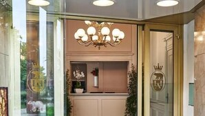 The entrance of Hotel Astoria with a glass door, a chandelier, and a reception desk with a plant. - Hotel Astoria (Biella)