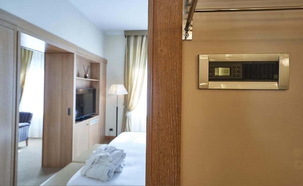 Una habitación de hotel con cama, televisor, armario y termostato en la pared.