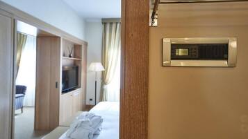 A hotel room with a bed, a TV, a wardrobe, and a wall-mounted thermostat.