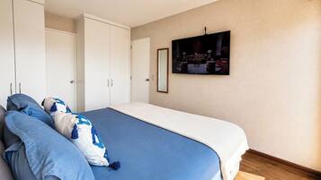 A bedroom with a large bed, white wardrobe, and a television mounted on the wall.