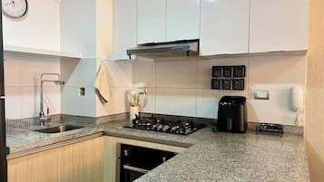 A modern kitchen with white cabinets, a stainless steel sink, a gas stove, and a coffee maker.