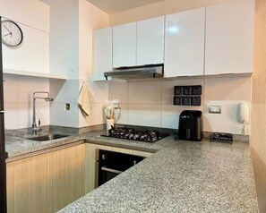 Una cocina moderna con armarios blancos, un lavamanos de acero inoxidable, una estufa a gas y una cafetera.