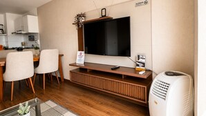 A modern living room with a flat-screen TV, a dining area with chairs, a kitchen in the background, and a white air purifier. - APT LOCK - LINCE (Lima)