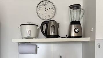 A kitchen with a granite countertop, a sink, a stove, a clock, a kettle, a blender, and a dish rack.