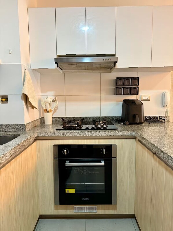 Una cocina con gabinetes blancos, una campana extractora de acero inoxidable, un horno empotrado y una encimera con una cafetera.