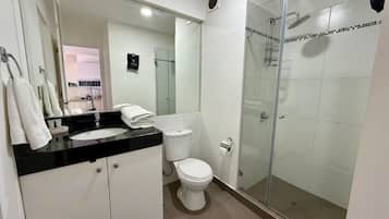 Un baño moderno con ducha envuelta en vidrio, inodoro blanco y lavamanos con encimera negra.