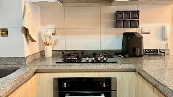 Una cocina con gabinetes blancos, una campana extractora de acero inoxidable, un horno empotrado y una encimera con una cafetera.