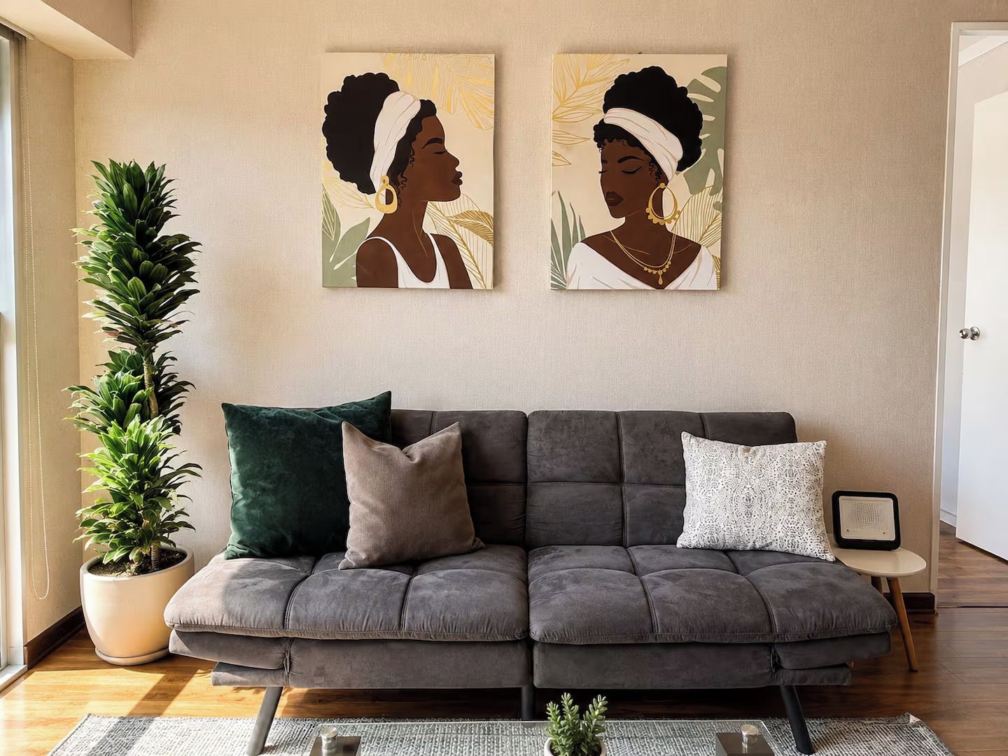 Un salon avec un canapé gris, une plante en pot et deux œuvres d’art murales.
