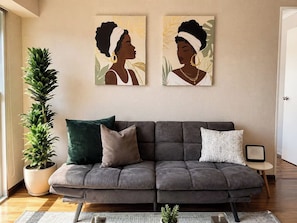Un saló amb un sofà gris, una planta en test i dues obres d'art murals.
