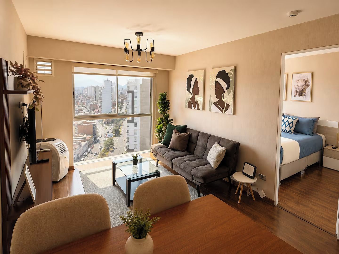 A modern living room with a sofa, coffee table, and dining table. There is a large window with a view of the city.