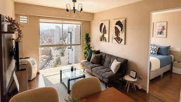 Una sala moderna con un sofá, una mesa de centro y una mesa de comedor. Hay una ventana grande con vista a la ciudad.