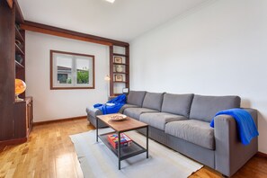 Una sala de estar con un sofá gris, una mesa de centro de madera, una estantería y un ventanal con vistas a zonas verdes.