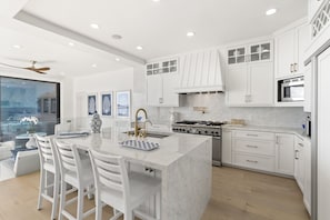 A modern kitchen with white cabinetry, a central island with bar stools, a gas stove, and a microwave. - Luxury on the Beach, Brand New Listing! (Oceanside)