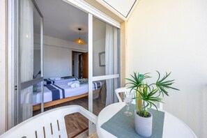 Ein Balkon mit einem Bett, einem Tisch mit einer Pflanze und einer hängenden Lampe.