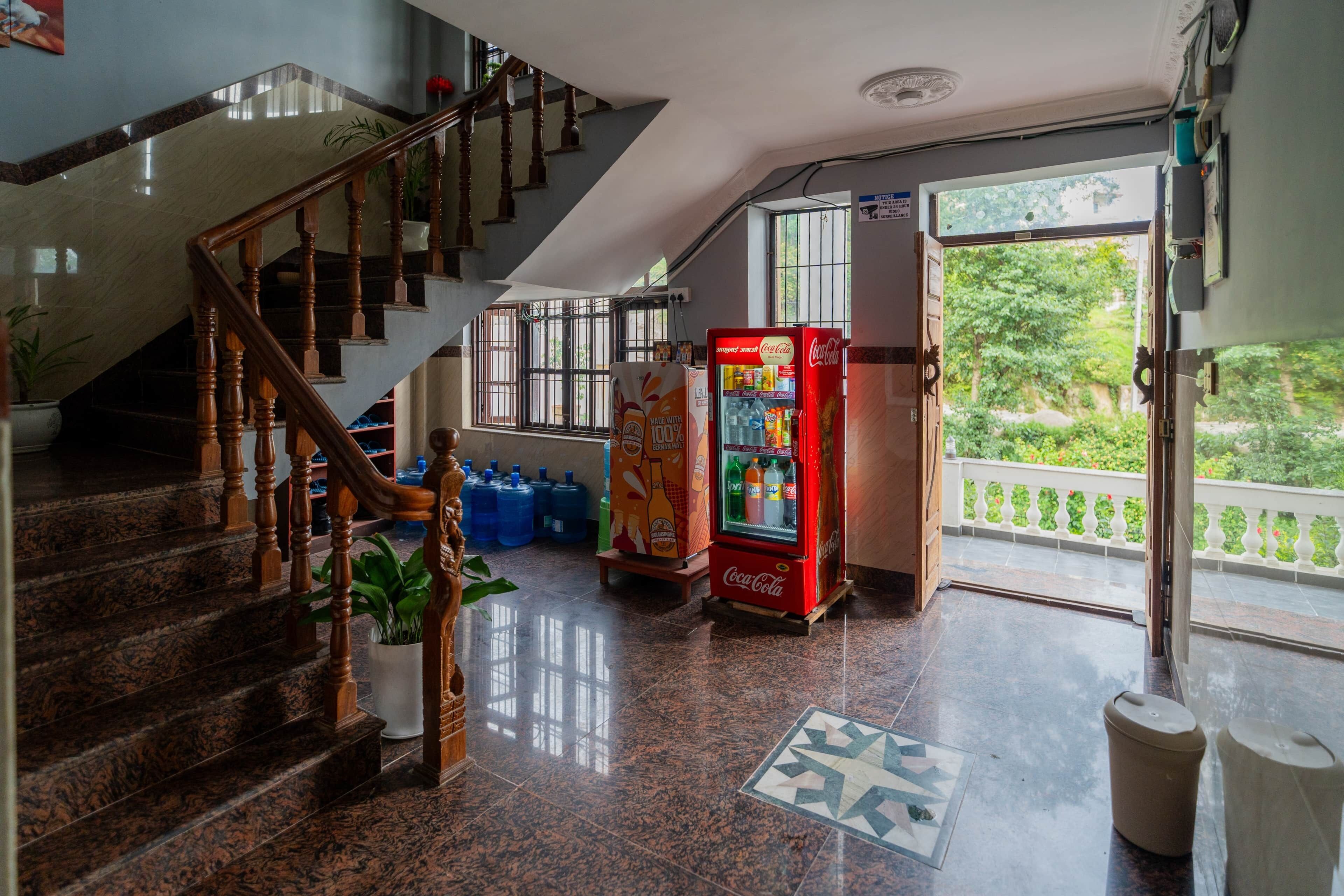 Una escalera con balaustres de madera, un refrigerador Coca-Cola y vista a zonas verdes al exterior.