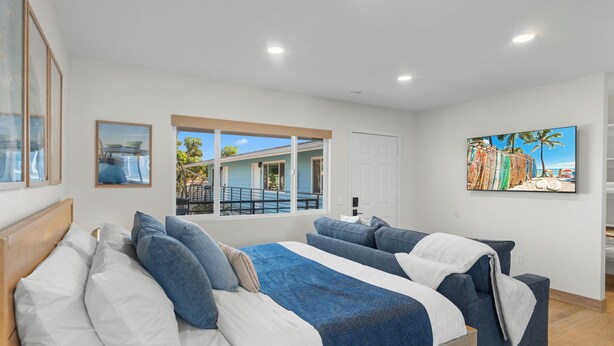 A bedroom with two beds, a large window, a painting, and a view of the outside.