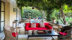 Un patio exterior con mobiliario de mimbre, un sofá rojo y plantas en macetas.
