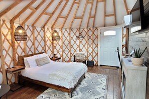 A cozy bedroom with a wooden bed, two hanging lamps, a white door, and a small table with a plant.