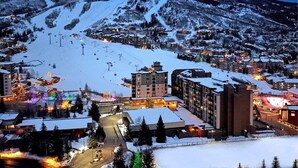 Eine verschneite Bergstadt im Abendlicht, mit beleuchteten Gebäuden und einer Seilbahn im Hintergrund.