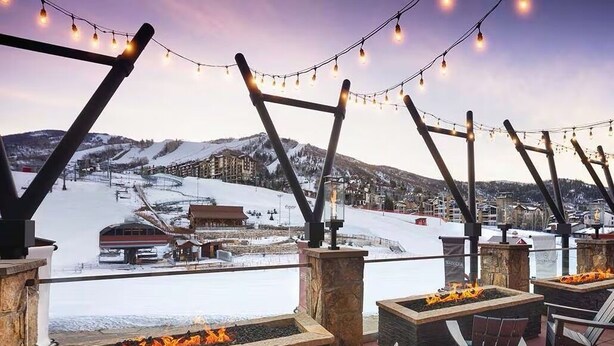 Eine Terrasse mit Sitzgelegenheiten im Freien und Feuerstellen mit Blick auf eine verschneite Landschaft und einen Skiort.