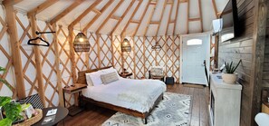 A cozy bedroom with a wooden bed, a small bedside table, a chair, and a hanging light fixture.