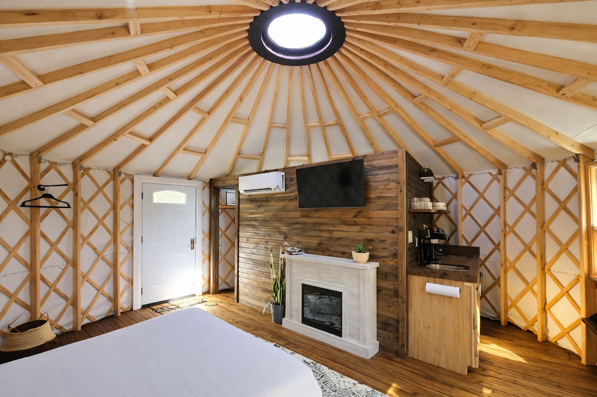 A yurt with a central hearth, a mounted television, and a wooden lattice wall.