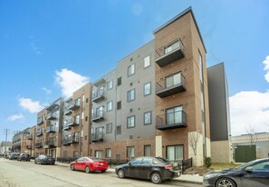 Un immeuble résidentiel à plusieurs étages, doté de balcons, d’un parking et surplombant un ciel dégagé.