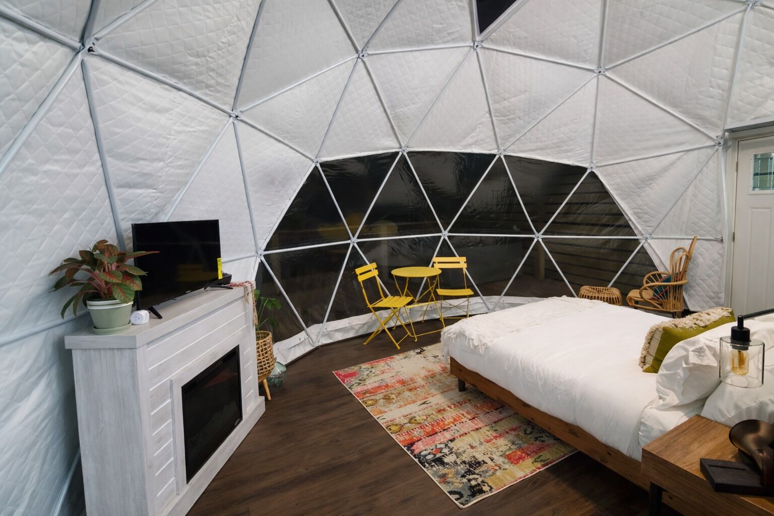 Habitación tipo tienda de campaña con cama, televisión, chimenea y zona de estar con sillones.