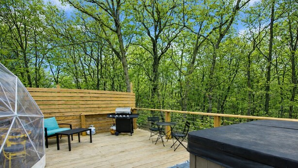 Un patio in legno con barbecue, posti a sedere all'aperto e una vasca idromassaggio.