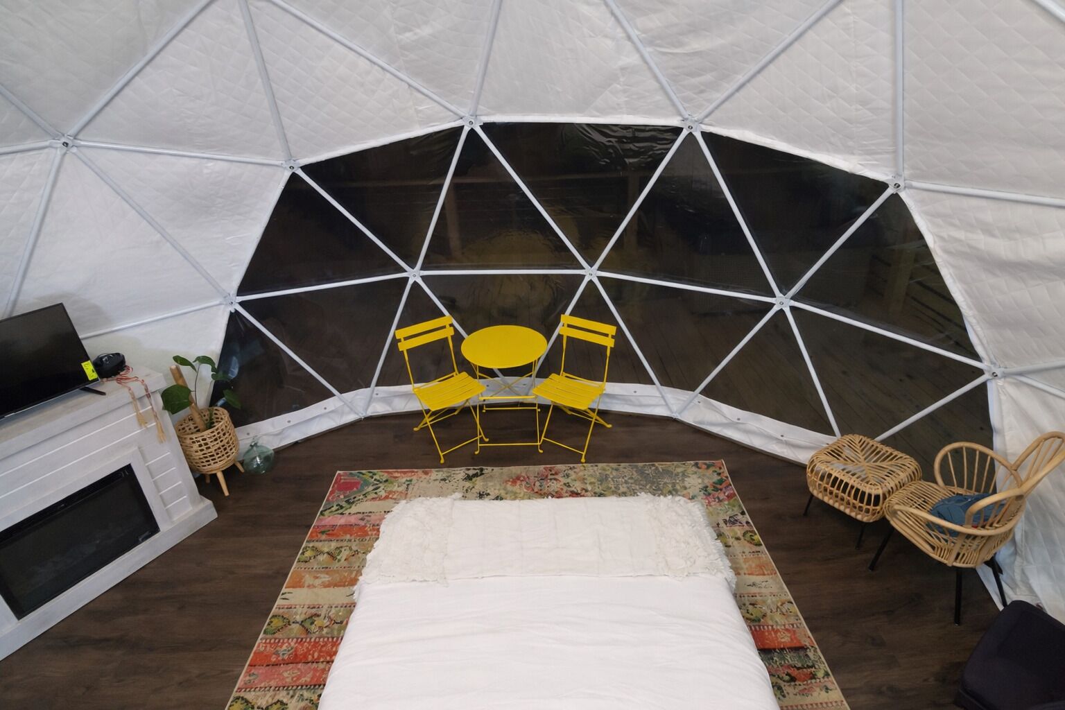 Una tenda con un camino, sedie gialle, un letto e una poltrona in vimini.
