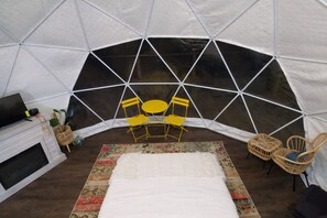 A tented room with a fireplace, yellow chairs, a bed, and a woven chair. - The Penguin Igloo: Unique Geodesic Dome + Hot Tub (Logan)