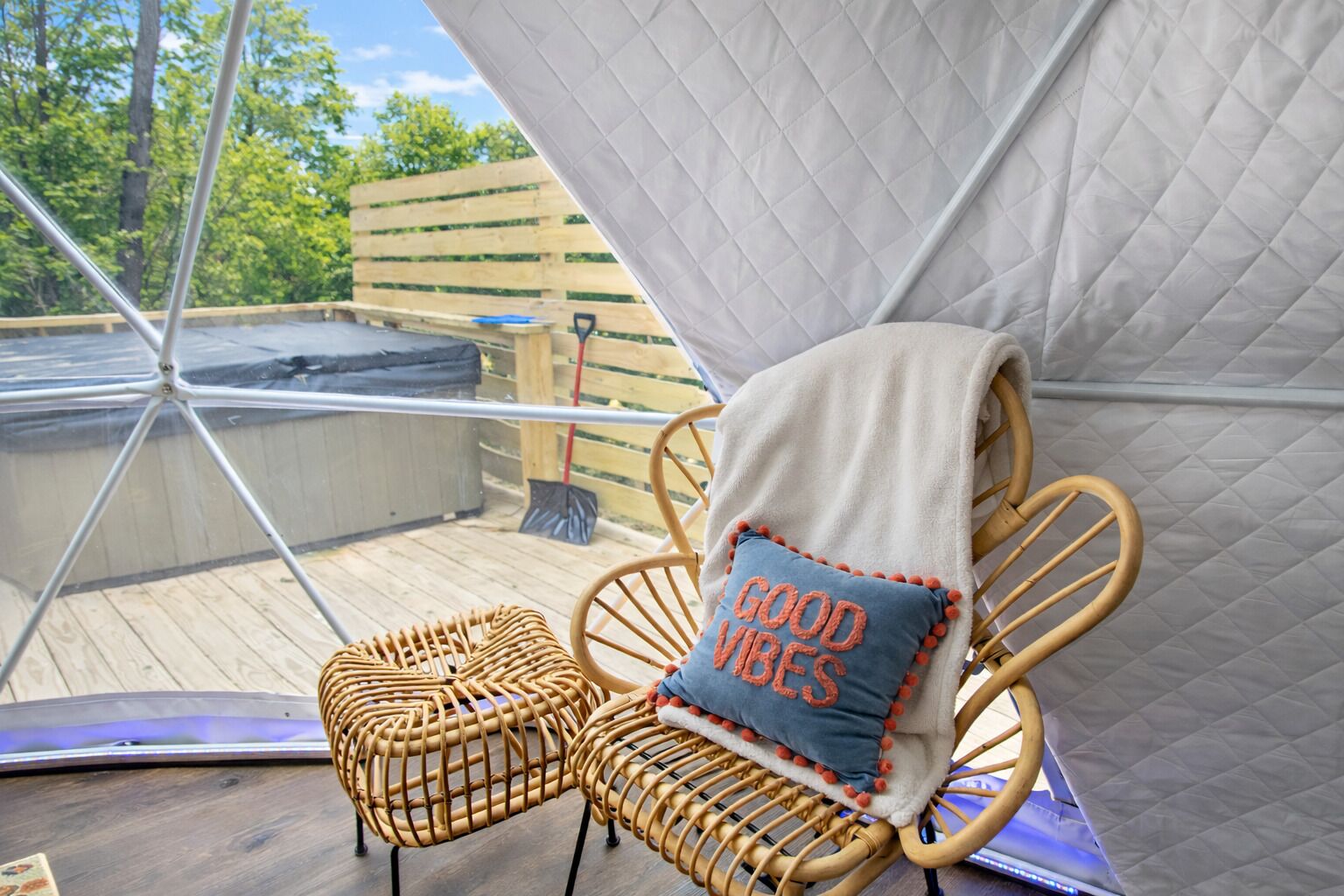Une chaise en osier avec un coussin, une structure blanche en forme de tente et une terrasse en bois.