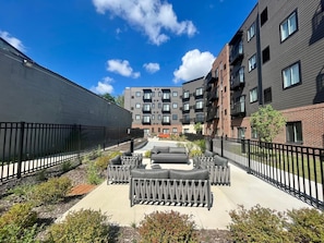Un patio con mobiliario exterior, un brasero en el centro y vistas de edificios de varios pisos al fondo.