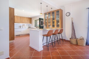 A modern kitchen with a central island, wooden cabinets, and a tiled floor. - Villa Dos Amores - Heated swimming pool (Azeitão)