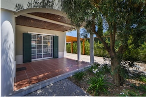 A modern house with a covered porch, a large sliding glass door, and a garden area with trees and plants. - Villa Dos Amores - Heated swimming pool (Azeitão)