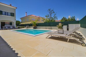 A swimming pool with lounge chairs and a covered area, surrounded by a fence and a building with a red-tiled roof. - Villa Dos Amores - Heated swimming pool (Azeitão)