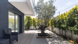 Een modern buitenterras met een zithoek, een grote plantenbak en uitzicht op een woonstraat.