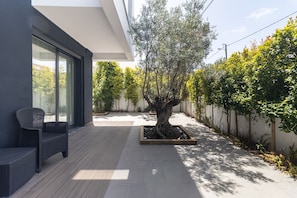 Eine moderne Außenpatio mit Sitzgelegenheit, einem großen Baumkübel und Blick auf eine Wohnstraße.