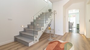 Een moderne trap met glazen balustrades, een houten vloer en een klein tafeltje met een vaas.