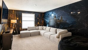 A room with a sectional sofa, a flat-screen TV, a lamp, and a wall mural of a castle. - 6BR Pool+Spa | The Retreat ChampionsGate | Disney 10 min (Davenport)