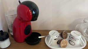 Une machine à café rouge et noire, avec un plateau rempli de tasses à café et des petits sachets de crème.