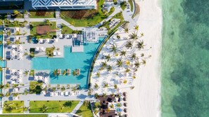 An aerial view of a resort with a central swimming pool, multiple lounge areas, and a beachfront. - 3BR Luxury Loft w/ Private Rooftop Jacuzzi (Q.R.)