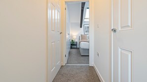 A narrow hallway with white doors leading to a bedroom with a bed and bedside table. - City Haven Liverpool | 3BR w/ Parking (Merseyside)