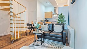 A modern living room with a black leather sofa, a round coffee table, and a spiral staircase. - City Haven Liverpool | 3BR w/ Parking (Merseyside)