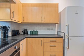 Een keuken met houten kastjes, een Bosch koelkast en een zwart aanrecht.