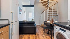 A compact kitchen with a washing machine, a dining area with a table and chairs, a black sofa, and a spiral staircase. - City Haven Liverpool | 3BR w/ Parking (Merseyside)