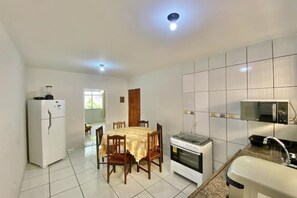 Een kleine keuken met een koelkast, fornuis en spoelbak, en een eethoek met stoelen en een tafel.