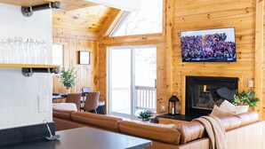 Una sala de estar moderna con chimenea, televisor montado en la pared y una zona de estar con sofá y sillones.